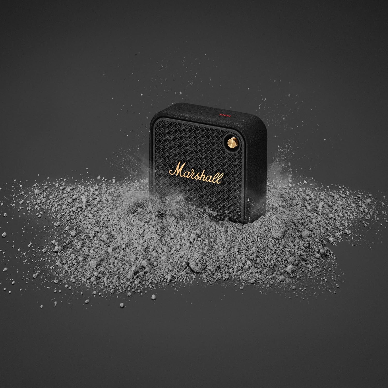 Marshall portable Bluetooth speaker with a rugged, dustproof design, showcased in a dusty environment, ideal for outdoor use.