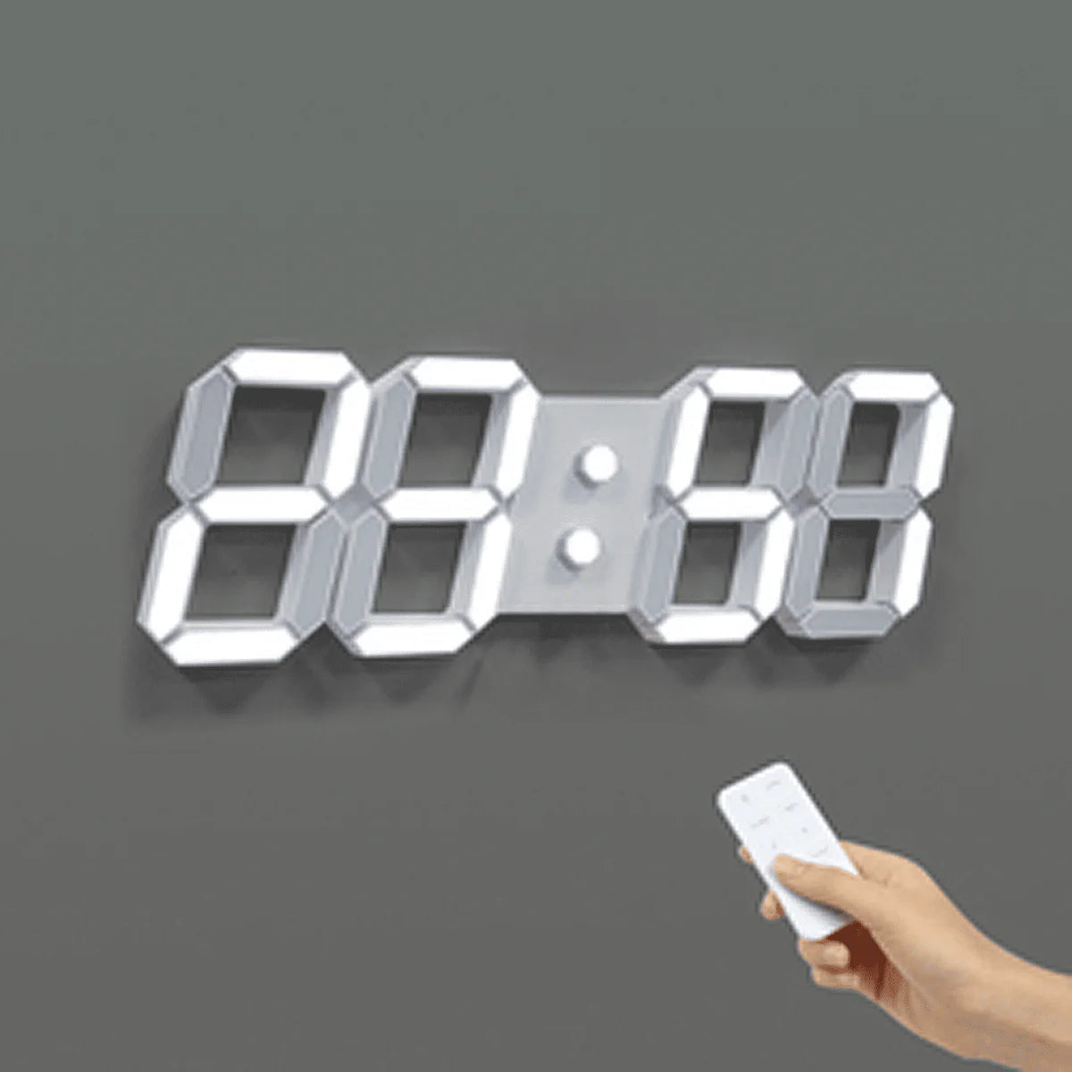  A digital wall clock with large illuminated numbers is mounted on a gray wall. The clock is displaying "88:88." A hand holding a remote control is aimed at the clock, indicating the use of the remote to set or adjust the clock. The clock has a modern design with bright, easy-to-read numbers.