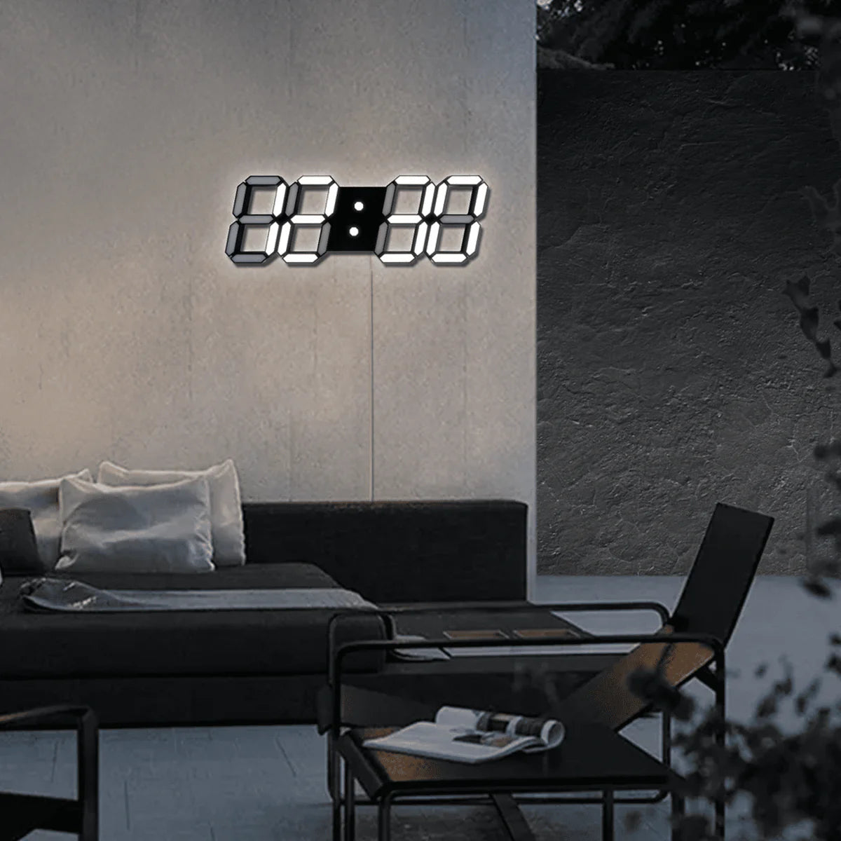 A minimalist outdoor lounge area featuring a modern black sofa with white cushions. A digital wall clock with large illuminated numbers is mounted on the wall above the sofa. In the foreground, a black metal coffee table holds a few magazines, and a black chair is positioned next to it. The setting is sleek and contemporary, with soft ambient lighting enhancing the relaxed atmosphere.