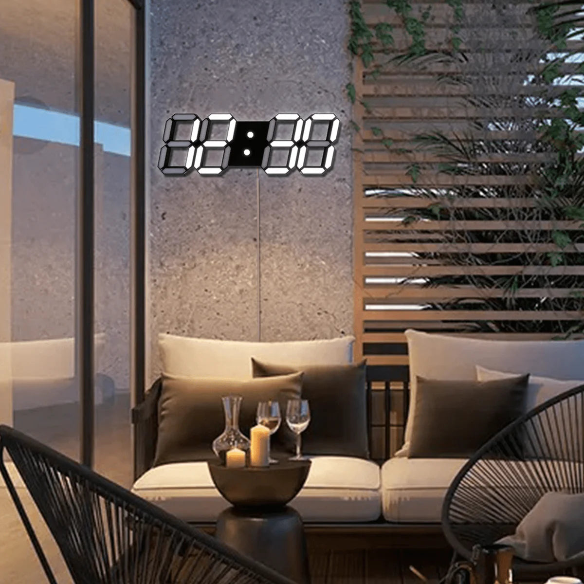 A stylish outdoor seating area featuring a beige cushioned sofa with several throw pillows. A digital wall clock with large illuminated numbers is mounted above the sofa. The setting includes a round coffee table with a candle and glasses, and a decorative wooden panel with green vines on the right side. The ambiance is cozy and inviting, with a modern touch highlighted by the soft lighting.