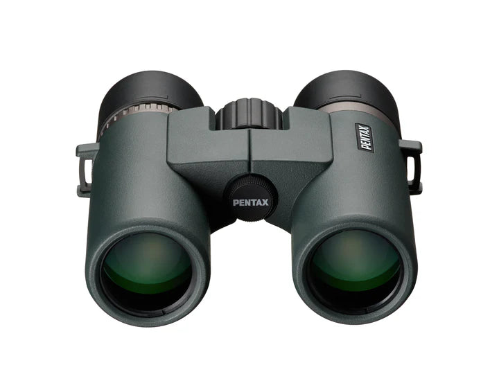  A front view of Ricoh Pentax AD 7x32 ED binoculars showing the large objective lenses with a greenish tint. The central hinge and focusing wheel are visible between the two barrels, with the Pentax branding on the right barrel. The binoculars have a robust, ergonomic design with a matte finish, emphasizing durability and high-quality optics for an enhanced viewing experience.