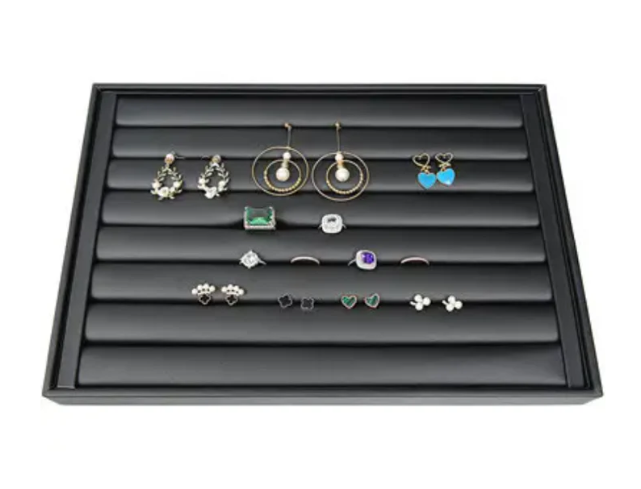 Jewelry organizer tray with velvet grooves displaying a collection of earrings and rings.