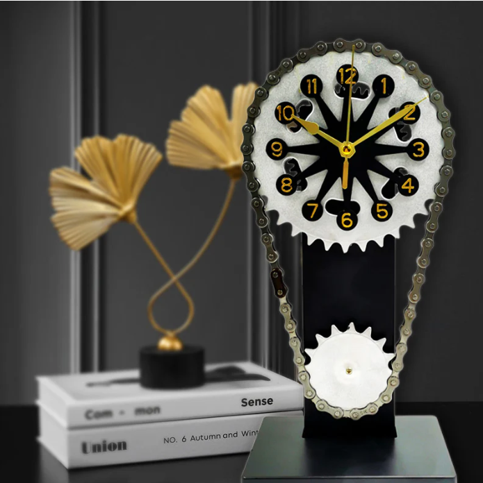 Unique gear-inspired clock with a chain-driven design, featuring gold-accented hands and numerals, set against a black backdrop with decorative golden sculptures and books in the background, adding a modern and industrial touch to the decor.