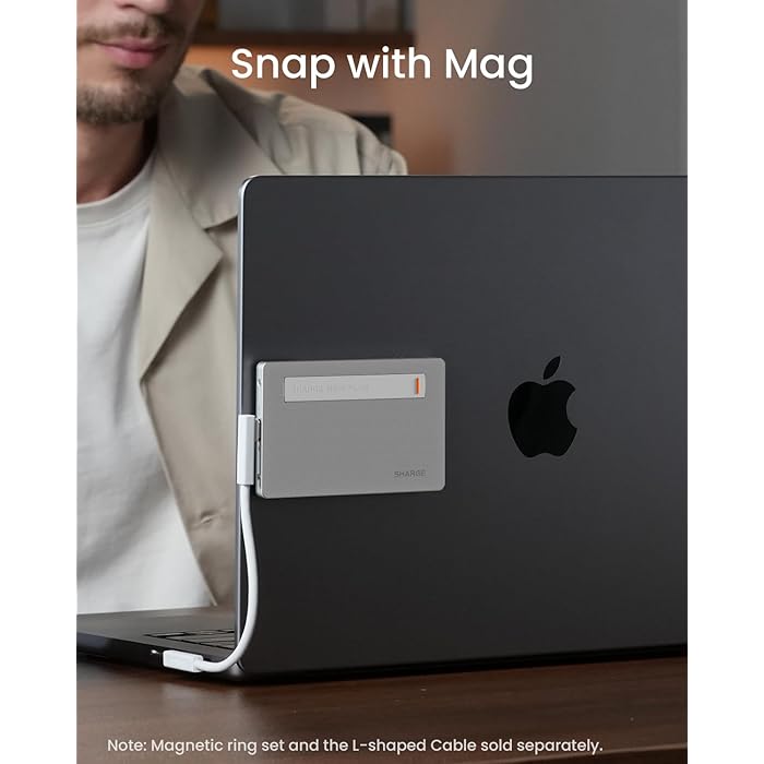 A SHARGE power bank magnetically attached to the back of a laptop, connected via a white cable. The setup highlights the "Snap with Mag" feature for secure attachment and convenient charging, with a note indicating that the magnetic ring set and L-shaped cable are sold separately.