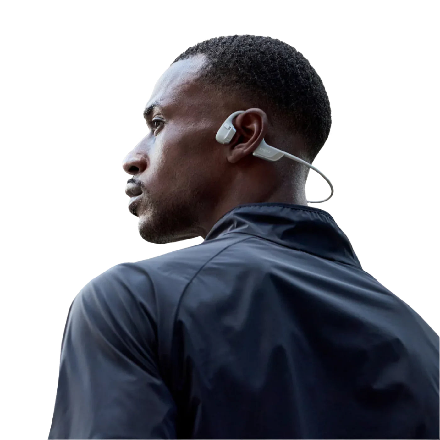 A man wearing a dark athletic jacket and wireless bone conduction headphones with a wraparound design. The headphones are light gray, with a sleek and ergonomic fit behind the ears. The background is transparent, emphasizing the focus on the person and the headphones.