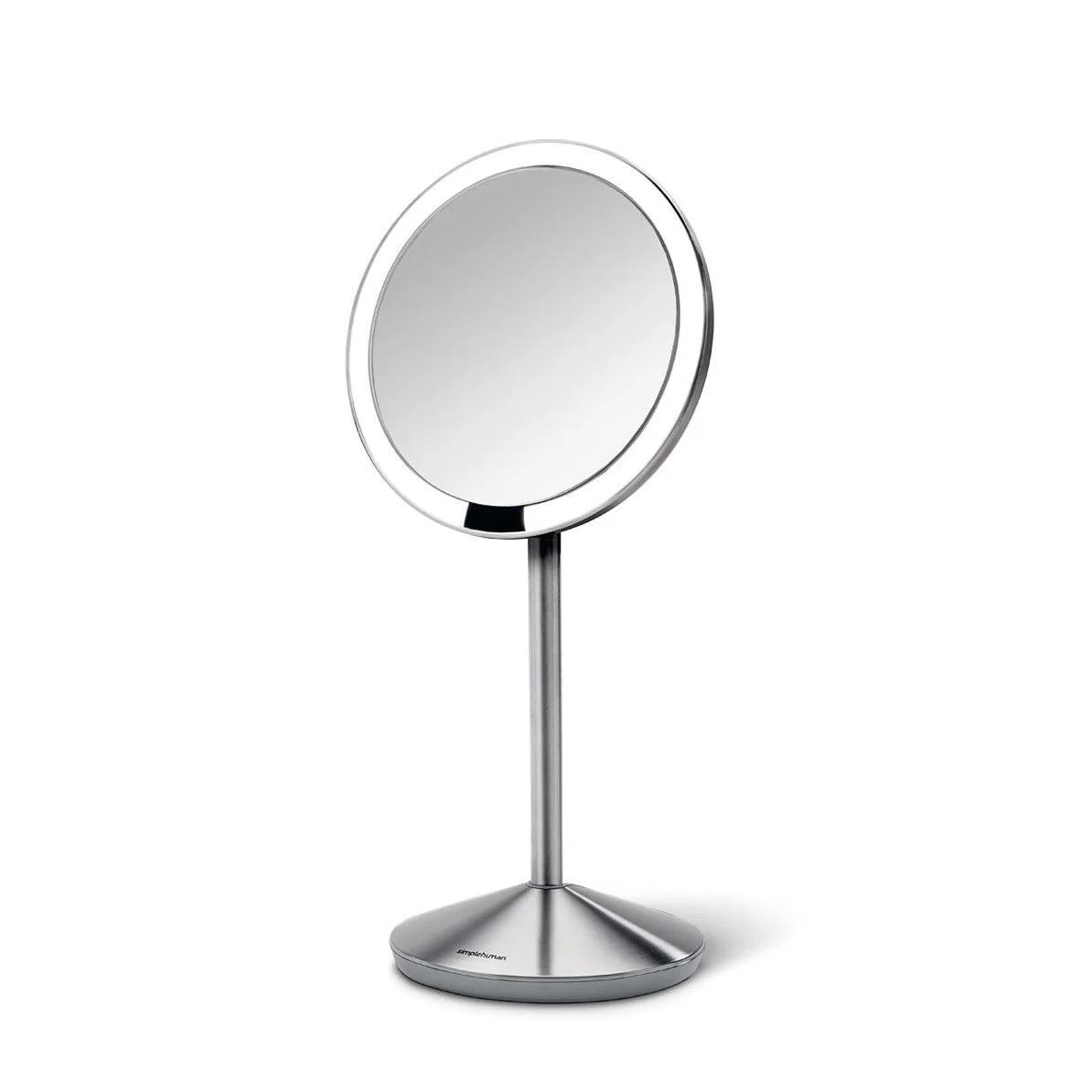  A side-angled view of a sleek, circular vanity mirror mounted on a slim, brushed stainless steel stand. The mirror has a thin bezel, offering a wide reflective surface with a modern and minimalist look. The base is conical and weighted, providing stability and matching the brushed metal finish of the stand. The design is contemporary and elegant, making it a stylish addition to a modern vanity or bathroom setting.