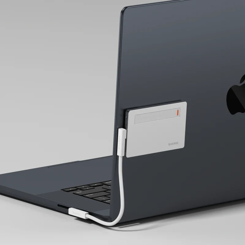 Slim metallic SHARGE power bank attached to the back of a laptop, connected via a white charging cable. The minimalist design complements the sleek look of the laptop, showcasing its lightweight and portable functionality for efficient charging.