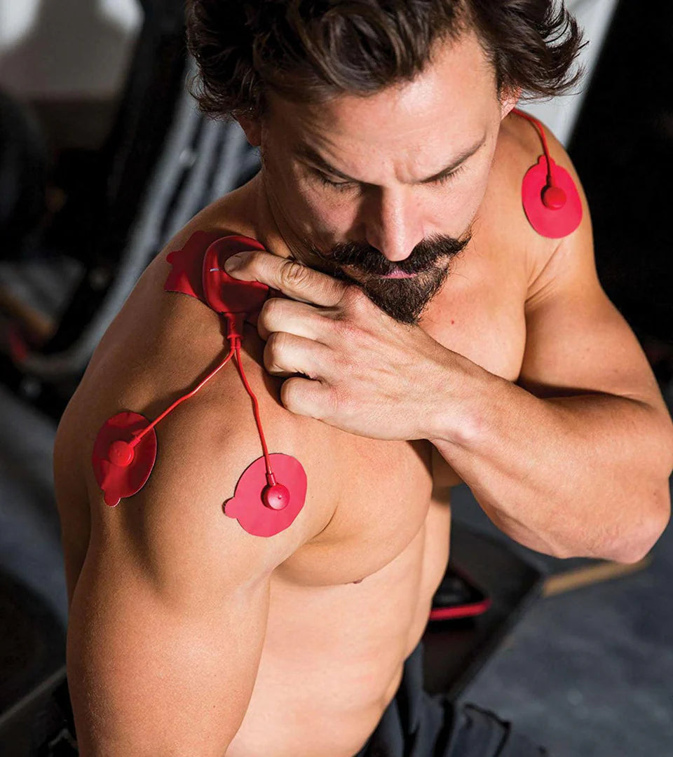 A man using red muscle stimulation pads on his shoulders and upper arms during a workout session, showcasing targeted muscle recovery and performance enhancement.