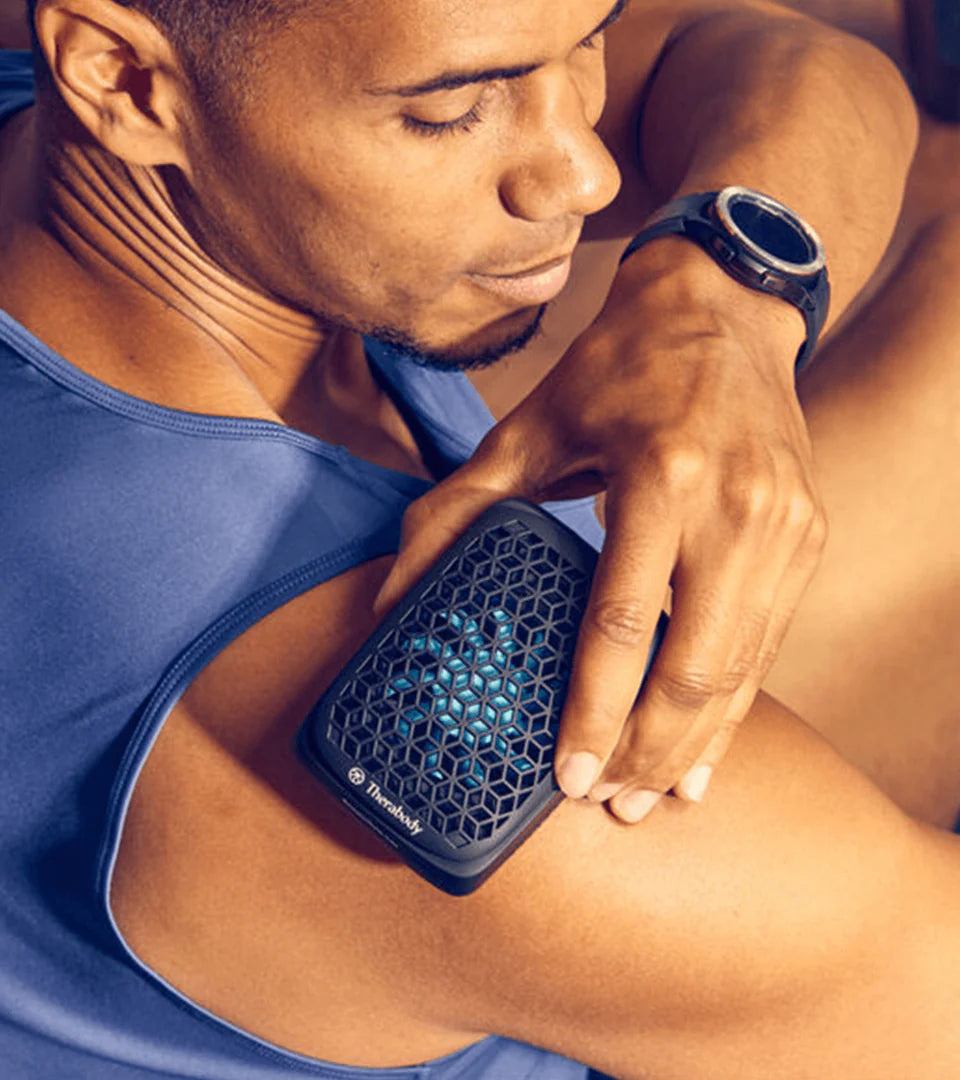 A man using a compact black muscle therapy device with a hexagonal mesh design on his shoulder, showcasing its portable and ergonomic design for targeted pain relief and muscle recovery.