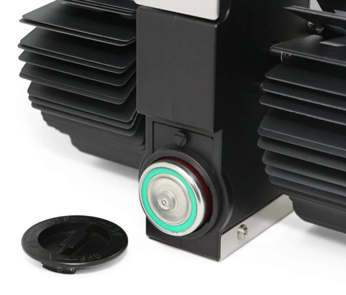 Close-up of a black mechanical component featuring a circular metallic button with a green ring and detailed heat sink fins. A detached black cap is shown nearby, emphasizing the functional and technical aspects of the design.