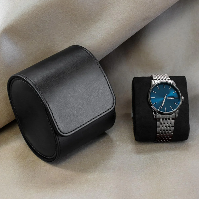 Black leather watch travel case displayed next to a wristwatch with a striking blue dial and a stainless steel bracelet, both set against a soft, neutral fabric background.