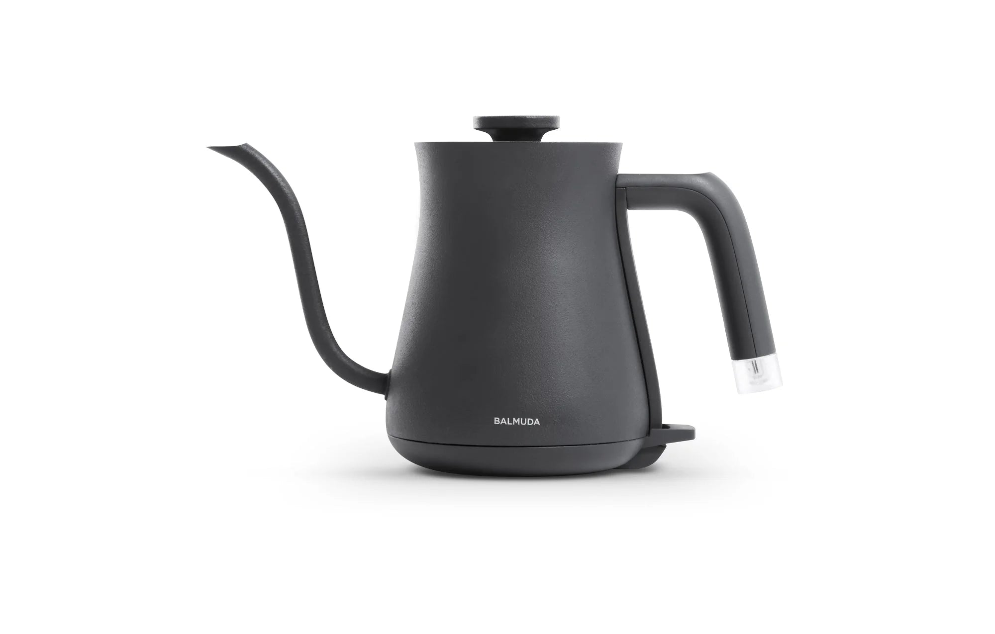  The image shows a Balmuda electric kettle in a matte black finish against a plain white background. The kettle features a sleek, minimalist design with a long, curved spout for precise pouring and a straight, ergonomic handle with a clear accent at the base.