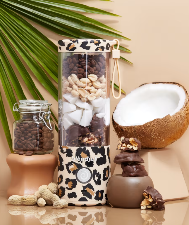 BlendJet 2 leopard print portable blender filled with coffee beans, peanuts, and coconut chunks, placed next to a coconut, peanuts, and a jar of coffee beans.