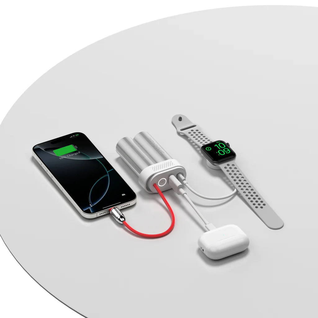 A SHARGE portable power bank charging multiple devices simultaneously, including a smartphone, smartwatch, and wireless earbuds. The power bank features a dual-cylinder metallic design with a red flexible charging cable and multiple output ports, demonstrating its capability to power different gadgets at once. The setup is displayed on a clean, white surface, emphasizing the power bank's compact and stylish design, ideal for modern tech users on the go.