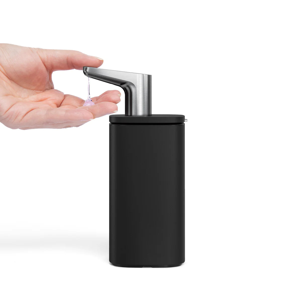 The image shows a hand underneath the nozzle of a sleek, black automatic soap dispenser, with soap being dispensed onto the hand. The dispenser has a modern design with a metallic nozzle that appears to be sensor-activated, releasing a precise amount of soap when a hand is detected. The branding and design suggest it is part of the Simplehuman product line, known for its high-quality, luxury home accessories.