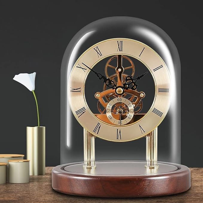 Elegant golden skeleton clock with visible inner gears and Roman numerals, encased in a clear glass dome and resting on a polished wooden base. The setup includes a simple white flower in a modern gold vase, adding a classic and refined touch to the decor.